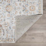 Close-up of the Dion Washable Floral Rug showing its charcoal, beige, and blue floral pattern and machine-woven construction. Fold