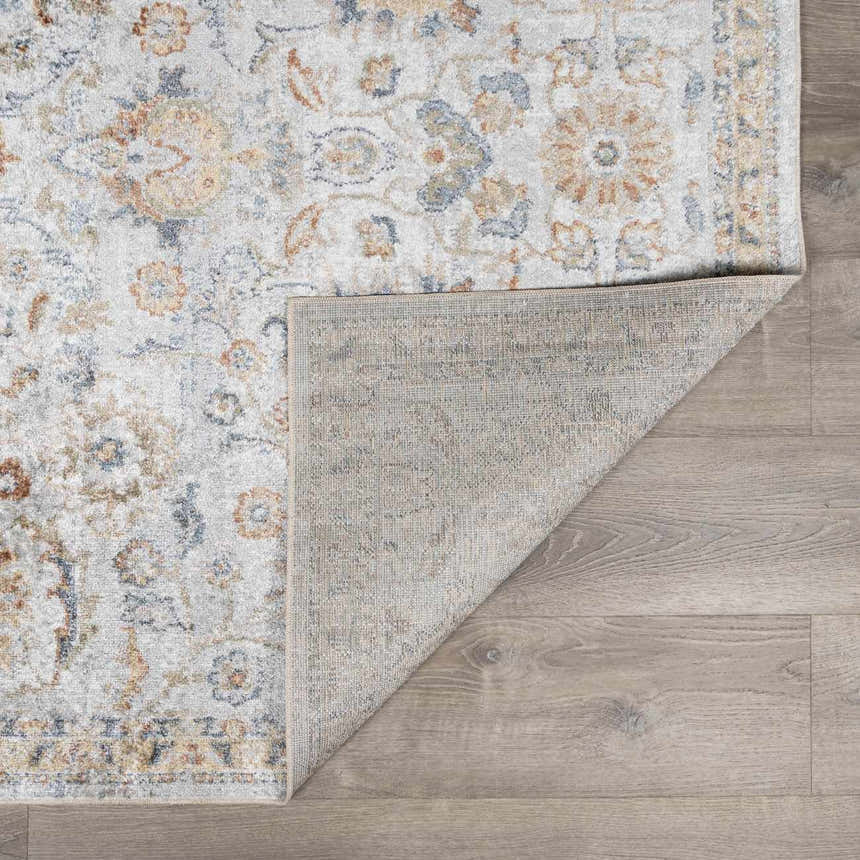 Close-up of the Dion Washable Floral Rug showing its charcoal, beige, and blue floral pattern and machine-woven construction. Fold