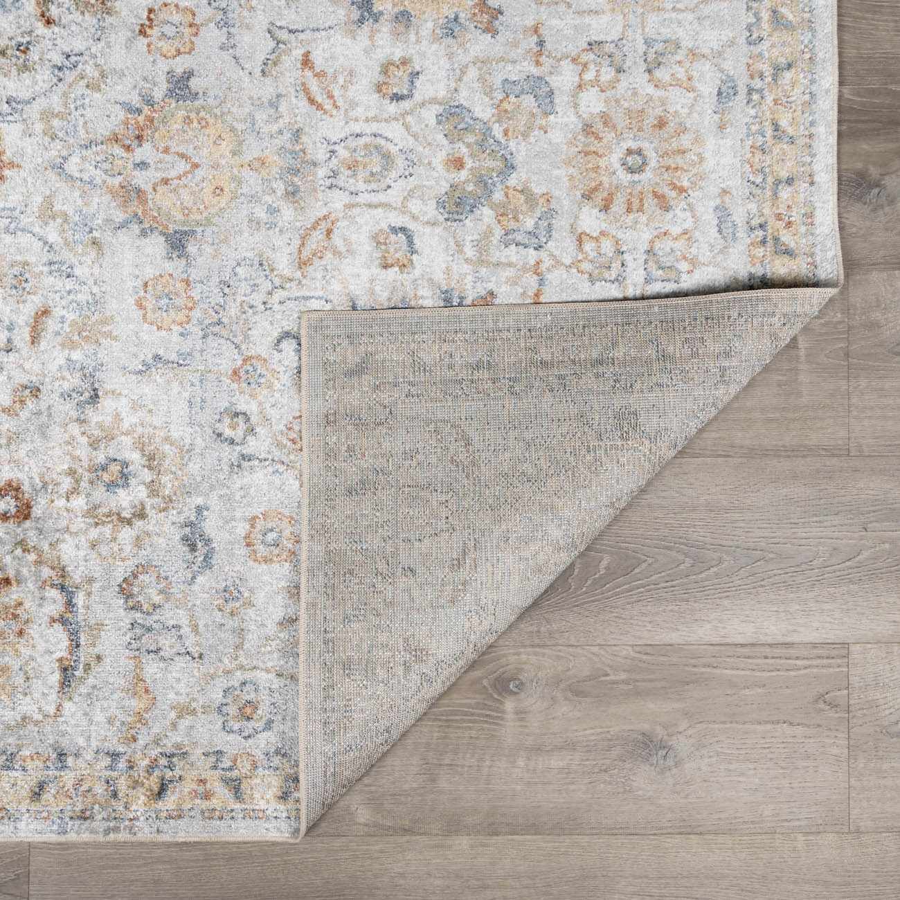 Close-up of the Dion Washable Floral Rug showing its charcoal, beige, and blue floral pattern and machine-woven construction. Fold