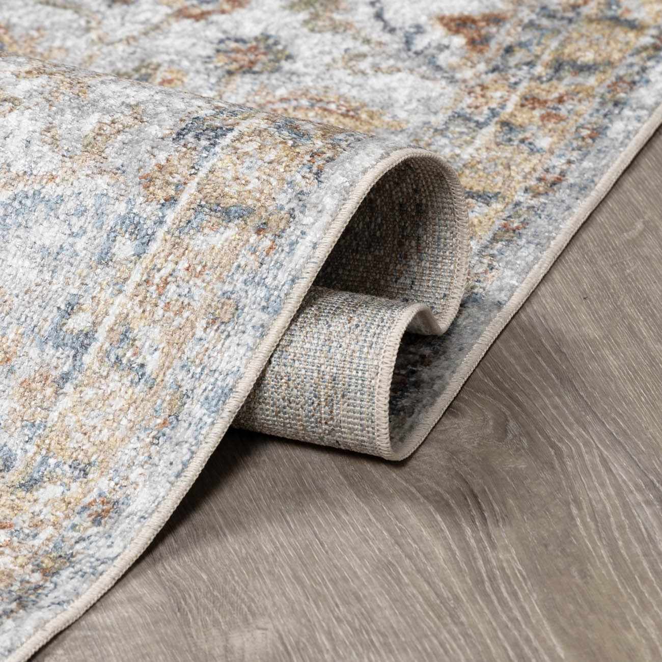 Close-up of the Dion Washable Floral Rug showing its charcoal, beige, and blue traditional pattern and soft texture. Fold