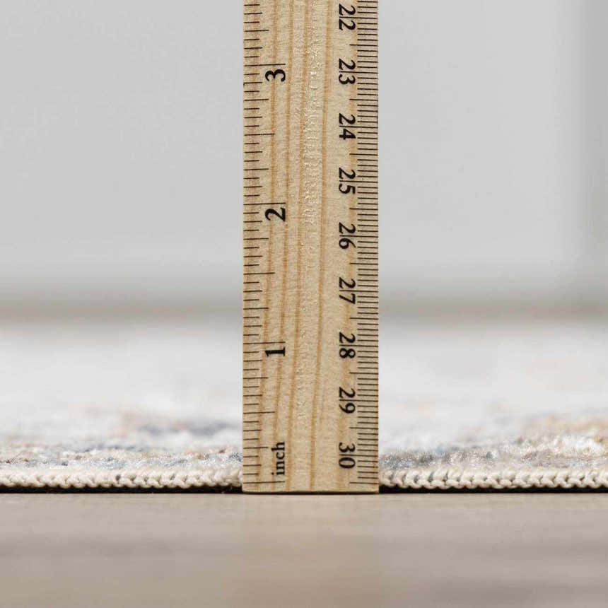 Close-up of the Dion Washable Floral Rug showing its pile height with a ruler. Neutral colors and machine-woven construction. Pile