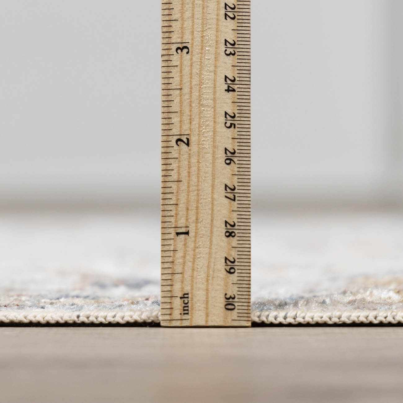 Close-up of the Dion Washable Floral Rug showing its pile height with a ruler. Neutral colors and machine-woven construction. Pile