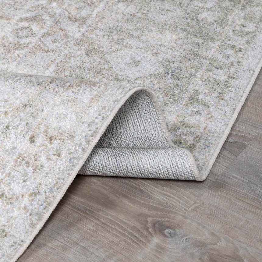 Close-up of the Gael Boutique Washable Rug showing its light blue, olive, and tan vintage pattern and machine-woven construction. Fold