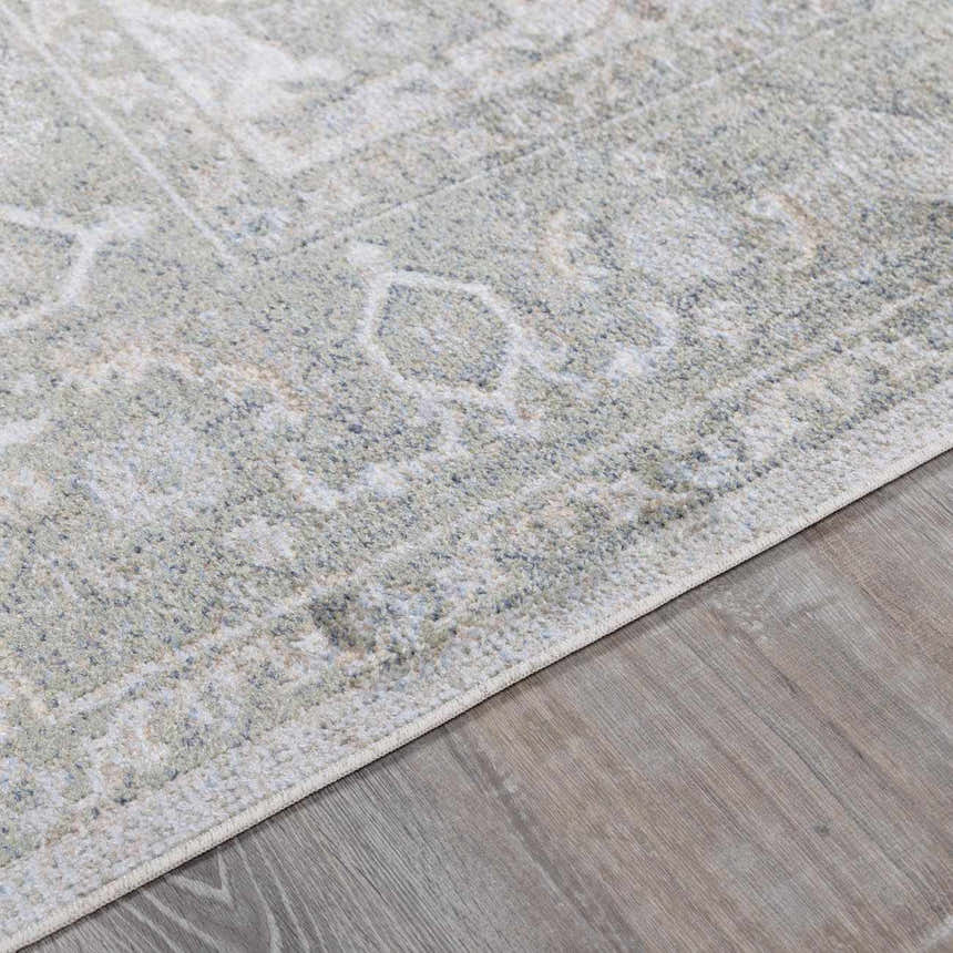 Close-up of Gael Boutique Washable Rug. Light blue, olive, tan, and yellow vintage pattern on a machine-woven polyester rug. Corner