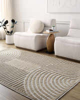 Living room scene with beige Deron Washable Area Rug, white chairs, wood side table, and modern decor. Roomscene-Rectangle