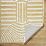Close up of the Deron Mustard Washable Area Rug. Beige geometric pattern on off-white background. Shows rug backing. Fold
