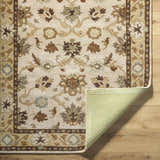 Close-up of the Smoot Area Rug. Beige wool rug with traditional floral pattern in brown, olive, and slate blue tones. Fold
