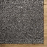 Close-up of the textured Sevan Black Wool Area Rug with jet black, medium gray, and taupe tones on wood floor. Corner