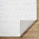 Close-up of the plush, white Hoshi Area Rug showing its shag texture and geometric pattern on wood flooring. Fold