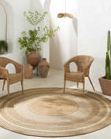 Boho-style room with a round Chael Flatweave Faux Jute Rug, wicker chairs, terracotta pots, and white textured walls. Roomscene-Round