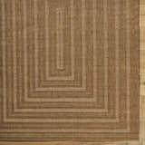Close-up of the Dyami Flatweave Faux Jute Rug. Features a geometric pattern and woven texture in camel and light brown tones. Corner