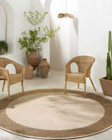 Neutral room scene with Inigo Flatweave Faux Jute Rug, wicker chairs, terracotta pots, and white textured walls. Roomscene-Round