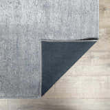 Close-up of the Isako Blue & Gray Solid Washable Area Rug showing its light gray color, texture, and dark gray backing. Fold