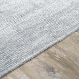 Close-up of the Isako Blue & Gray Solid Washable Area Rug showing texture and color on wood floor. Pile