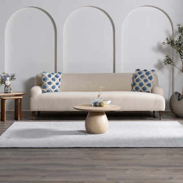 Living room scene with a light gray Isako Blue & Gray Solid Washable Area Rug, beige sofa, and round coffee table. Roomscene-Rectangle