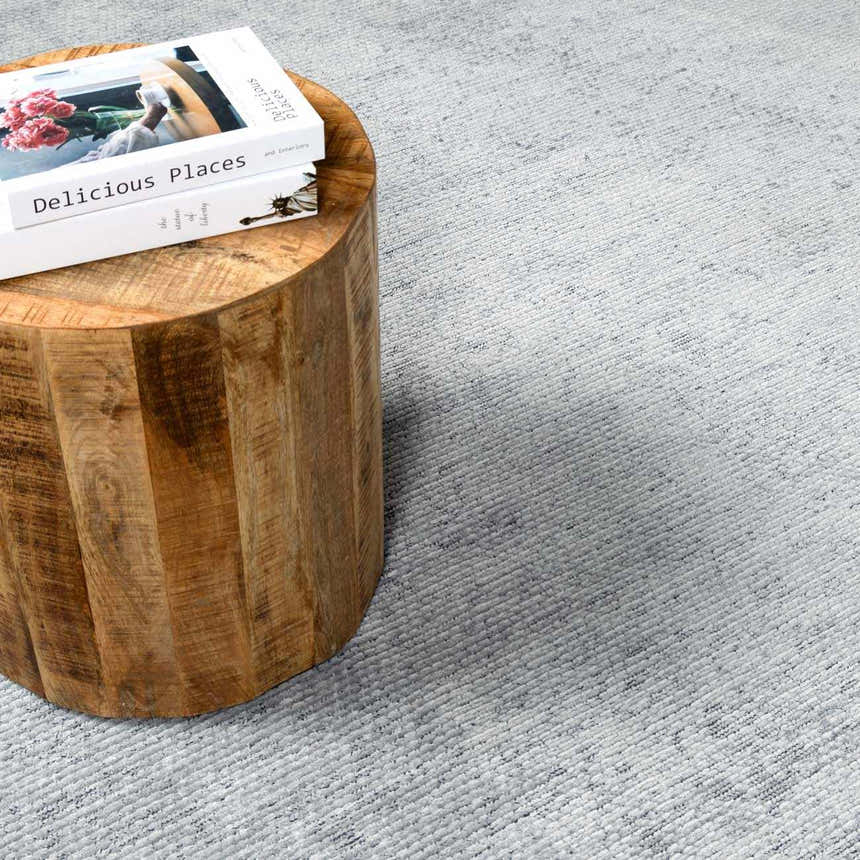 Close-up of the Isako Blue & Gray Solid Washable Area Rug with a subtle, textured design next to a wood side table. Styleshot