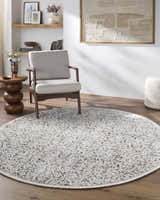 Living room scene with a round Haran Cloud Gray area rug, gray chair, wood side table, and neutral decor. Roomscene-Round