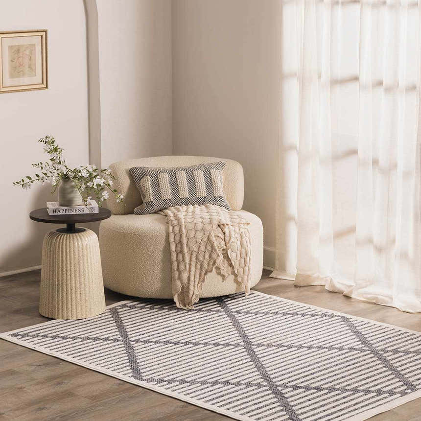 Cozy reading nook with a cream chair, side table, and the Anah Blue Outdoor Rug featuring a gray geometric pattern. Roomscene-Rectangle