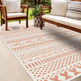 Outdoor patio scene with wooden furniture and a bone and clay colored Jove Orange Outdoor Rug. Roomscene-Rectangle