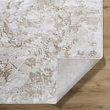 Close-up of the Jaren Tan Area Rug showing its beige, cream, and tan abstract pattern and texture on a wood floor. Fold