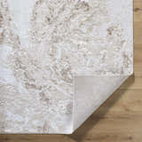 Close-up of the Kaleo Area Rug featuring a beige, cream, and tan contemporary pattern. Folded corner shows the rug's backing. Fold
