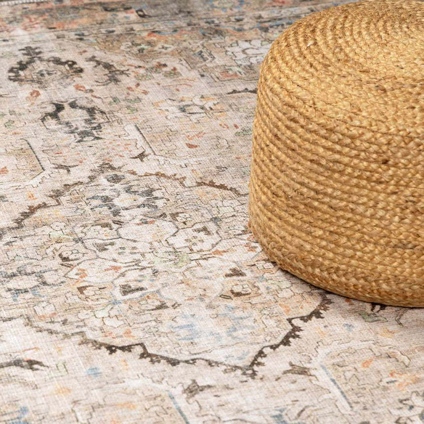 Close-up of Standon Vintage Flat Pile Washable Rug with oriental design in blue, charcoal, and dusty pink. Jute pouf on rug. Styleshot