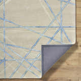 Close-up of the Hiba Area Rug: beige wool with a geometric blue line pattern. Hand-tufted rug with a gray backing. Fold