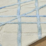 Close-up of Hiba Area Rug, a hand-tufted wool rug in beige with a blue geometric grid pattern. Soft texture. Texture