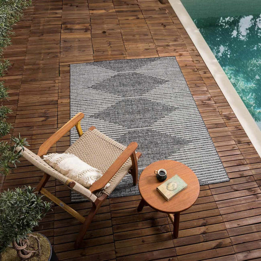 Outdoor scene with Stephan Area Rug in black, charcoal, and cream. Rug is styled by a pool with chair and side table. Roomscene-Rectangle