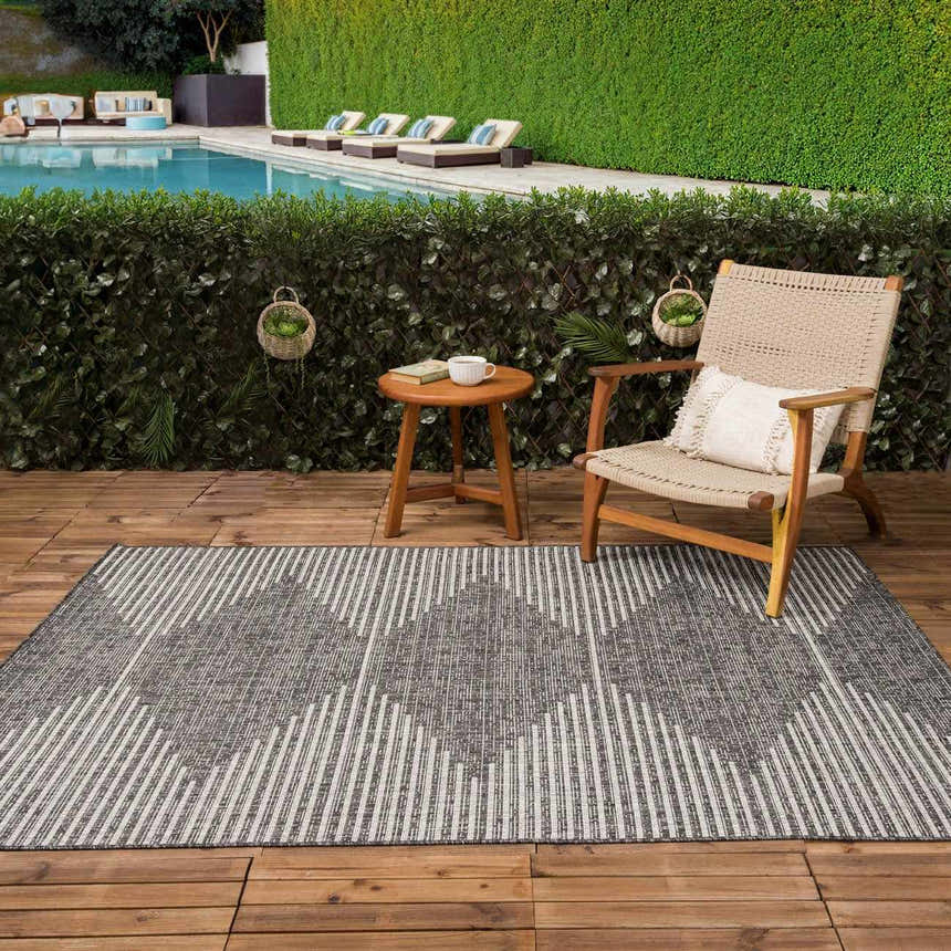 Outdoor patio scene with a gray and cream Stephan Area Rug, wood chair, and pool in the background. Roomscene-Rectangle