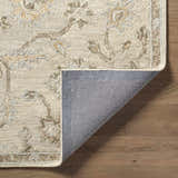 Close-up of the hand-tufted Adelle Oushak Area Rug. Beige wool rug with traditional floral pattern and gray backing on wood floor. Fold