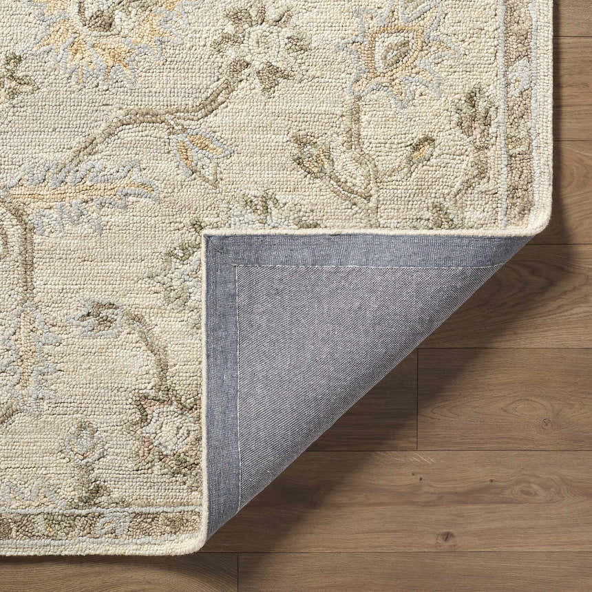 Close-up of the hand-tufted Adelle Oushak Area Rug. Beige wool rug with traditional floral pattern and gray backing on wood floor. Fold