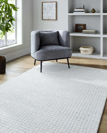 Living room scene with a gray chair on the soft blue checkered Anahid Area Rug. Neutral decor and light wood floors. Roomscene-Rectangle