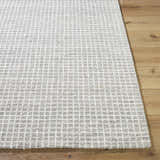 Close-up of the hand-tufted Anahid Gray Area Rug. Checkered pattern in ash, light silver, and off-white wool on wood floor. Front