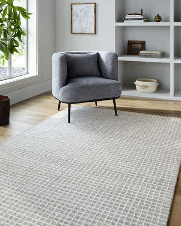Living room scene with gray chair and Anahid Gray Area Rug, a checkered wool rug in ash and off-white. Roomscene-Rectangle