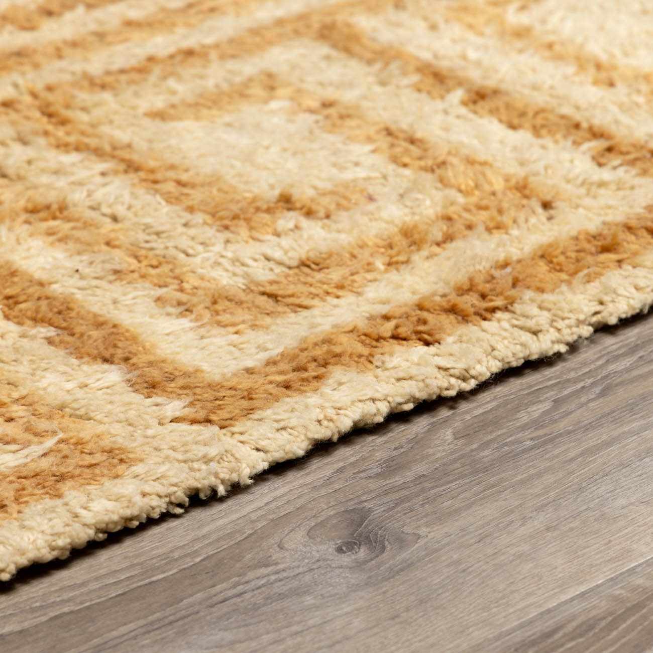 Close up of the hand tufted Wasim Area Rug, featuring a geometric pattern in camel and pearl wool. Pile