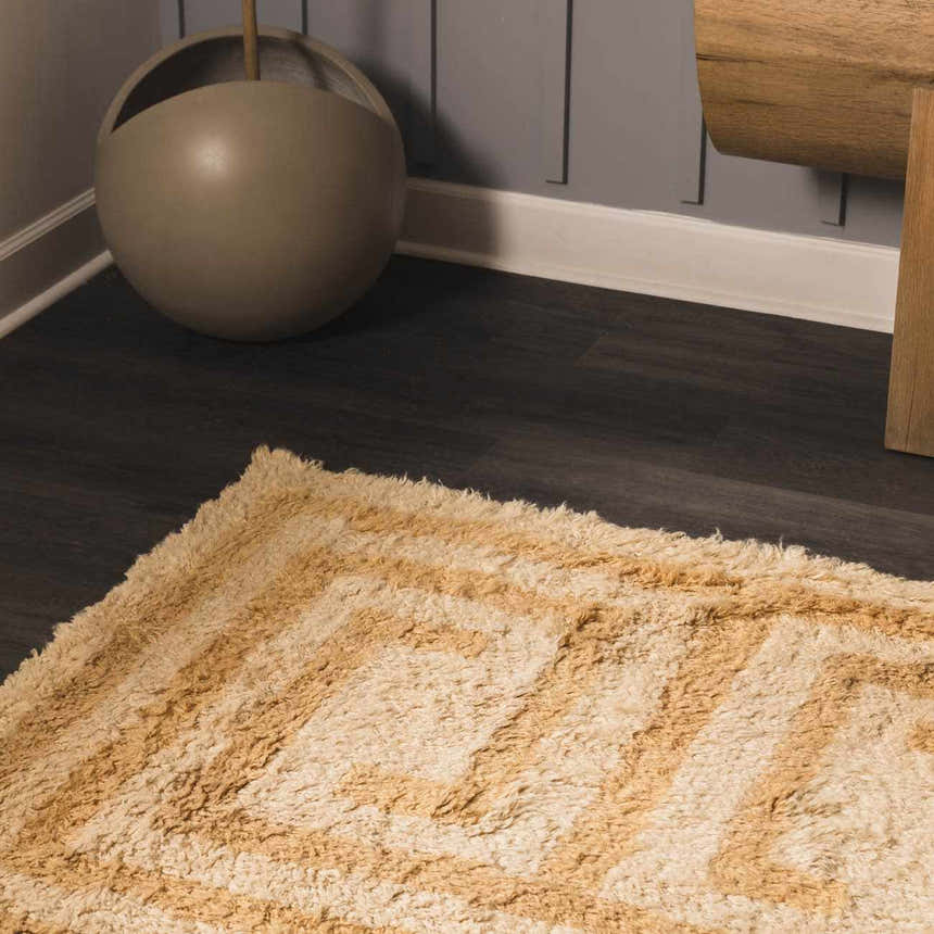 Close up of the tan and pearl Wasim Area Rug with a geometric pattern and shaggy texture. Corner
