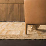 Close-up of the tan and pearl geometric design of the hand-tufted wool Wasim Area Rug next to a camel-colored chair. Styleshot