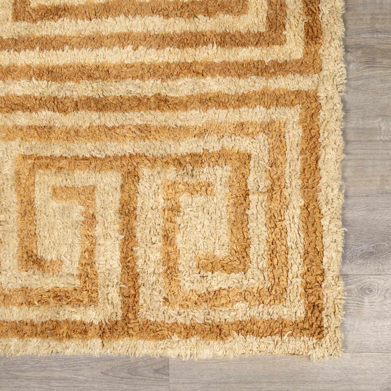 Close-up of the hand-tufted Wasim Area Rug. Wool rug features a geometric, maze-like pattern in tan and light wood tones. Swatch