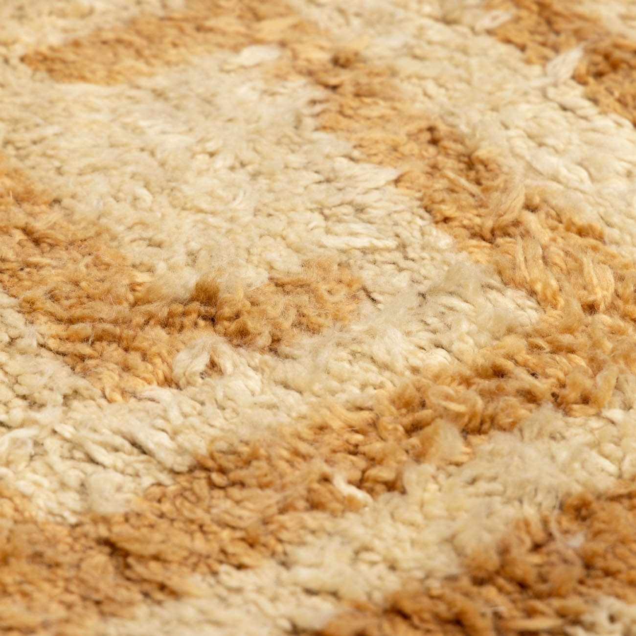 Close up of the hand-tufted Wasim Area Rug, showing its brick red, camel, and tan wool texture. Texture