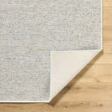 Close-up of Thanh Ivory Area Rug showing woven texture, neutral colors, and rug backing on wood floor. Fold