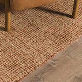 Close-up of Teresita Area Rug showing burnt orange and ivory wool texture under a chair on wood floor. Styleshot
