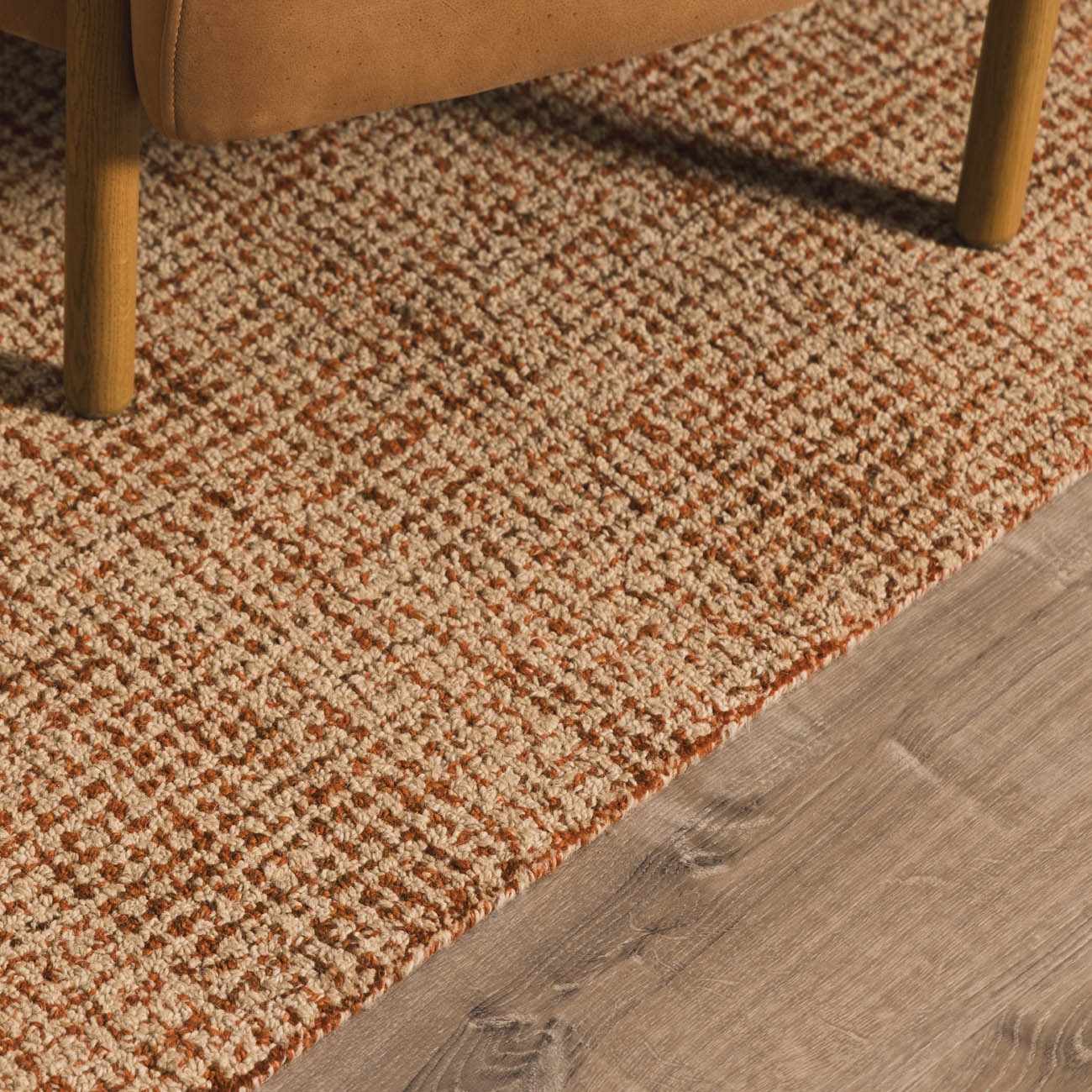 Close-up of Teresita Area Rug showing burnt orange and ivory wool texture under a chair on wood floor. Styleshot