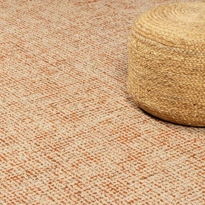Close-up of the Teresita Area Rug in burnt orange and ivory with a woven jute pouf. Hand-tufted wool texture. Styleshot
