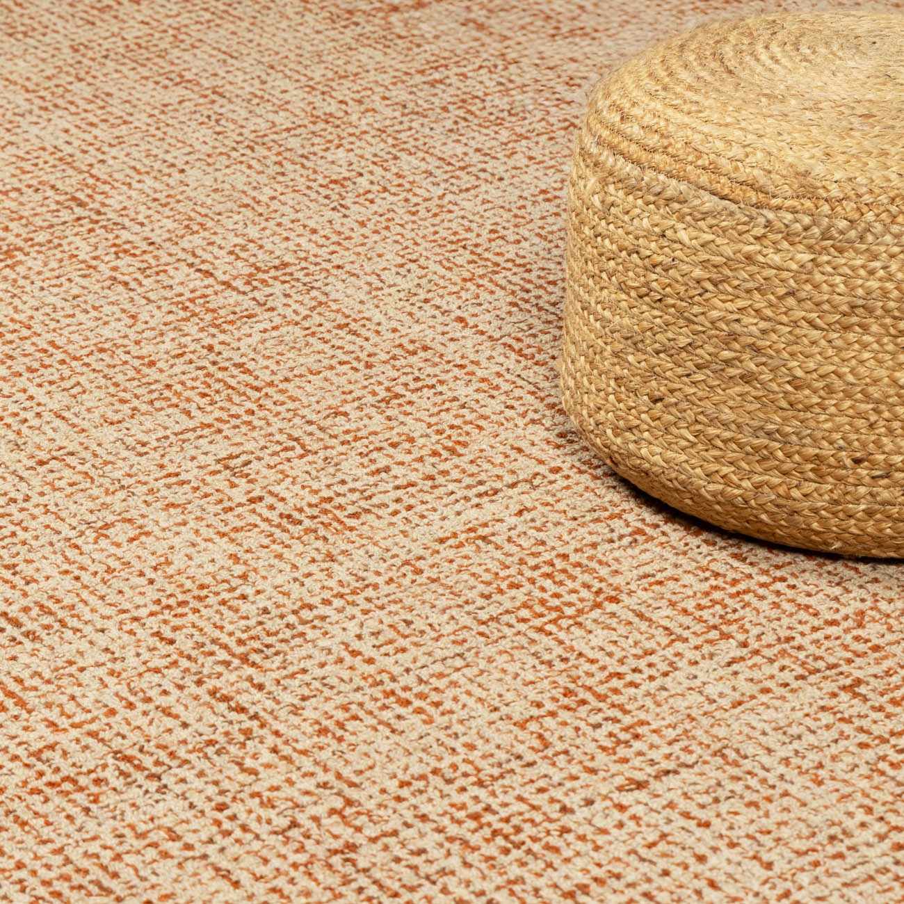 Close-up of the Teresita Area Rug in burnt orange and ivory with a woven jute pouf. Hand-tufted wool texture. Styleshot
