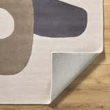 Close-up of the hand-tufted Terah Ivory Area Rug showing its charcoal, taupe, and ivory abstract design and wool texture. Fold