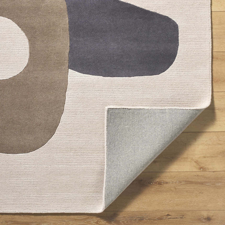 Close-up of the hand-tufted Terah Ivory Area Rug showing its charcoal, taupe, and ivory abstract design and wool texture. Fold