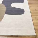 Close-up of the hand-tufted Terah Ivory Area Rug. Features charcoal, ivory, and taupe abstract shapes on a wool base. Front