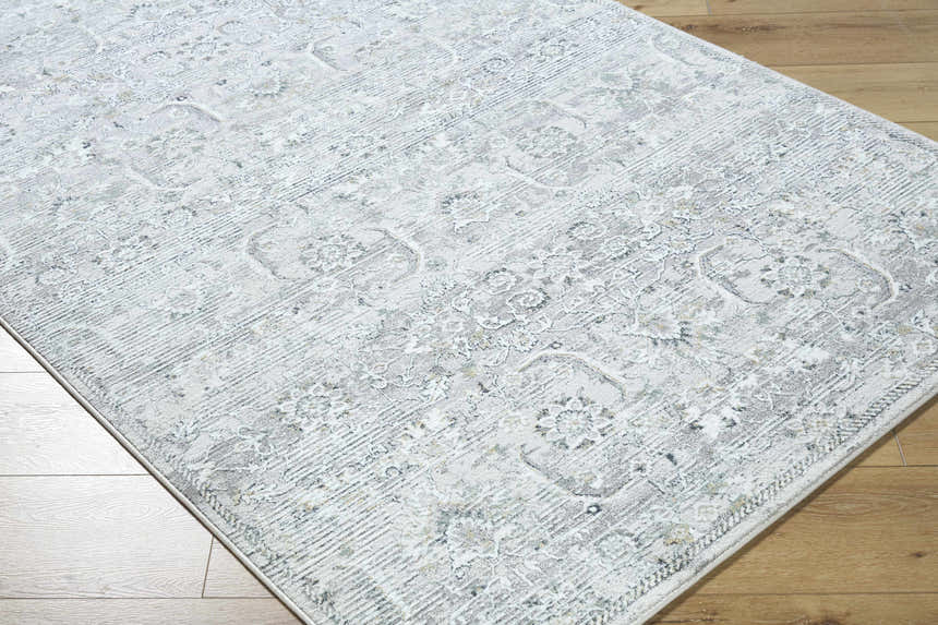 Close-up of Tariq area rug. Traditional floral pattern in silver gray, slate blue, and sterling gray on wood floor. Corner