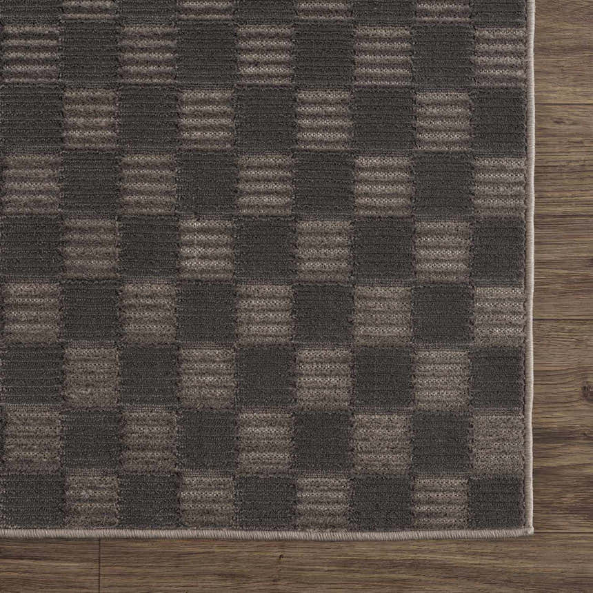 Close-up of the Truls 3D Checkered Washable Rug in Black and Gray. Features a textured, checkered pattern on a wood floor. Swatch